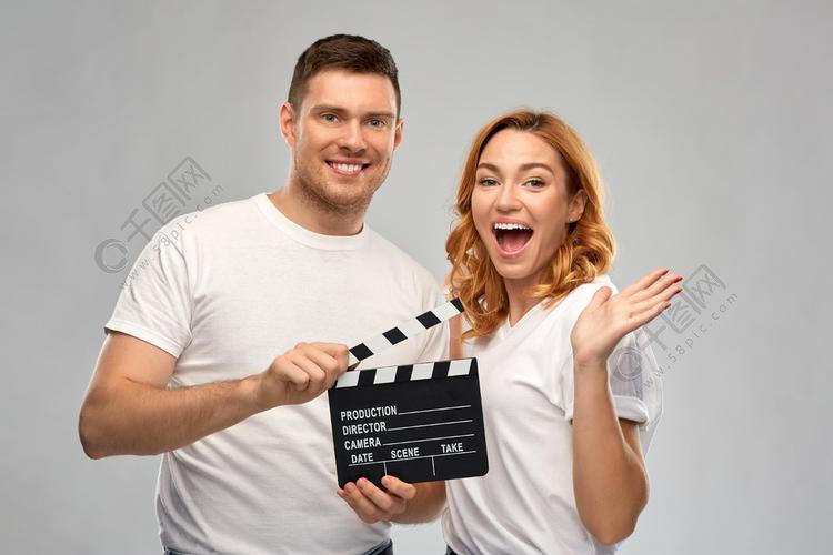 生产,电影摄制和娱乐概念-愉快的夫妇画象在白色t恤杉的有在灰色背景